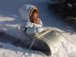 Cute black baby in a sled with snow